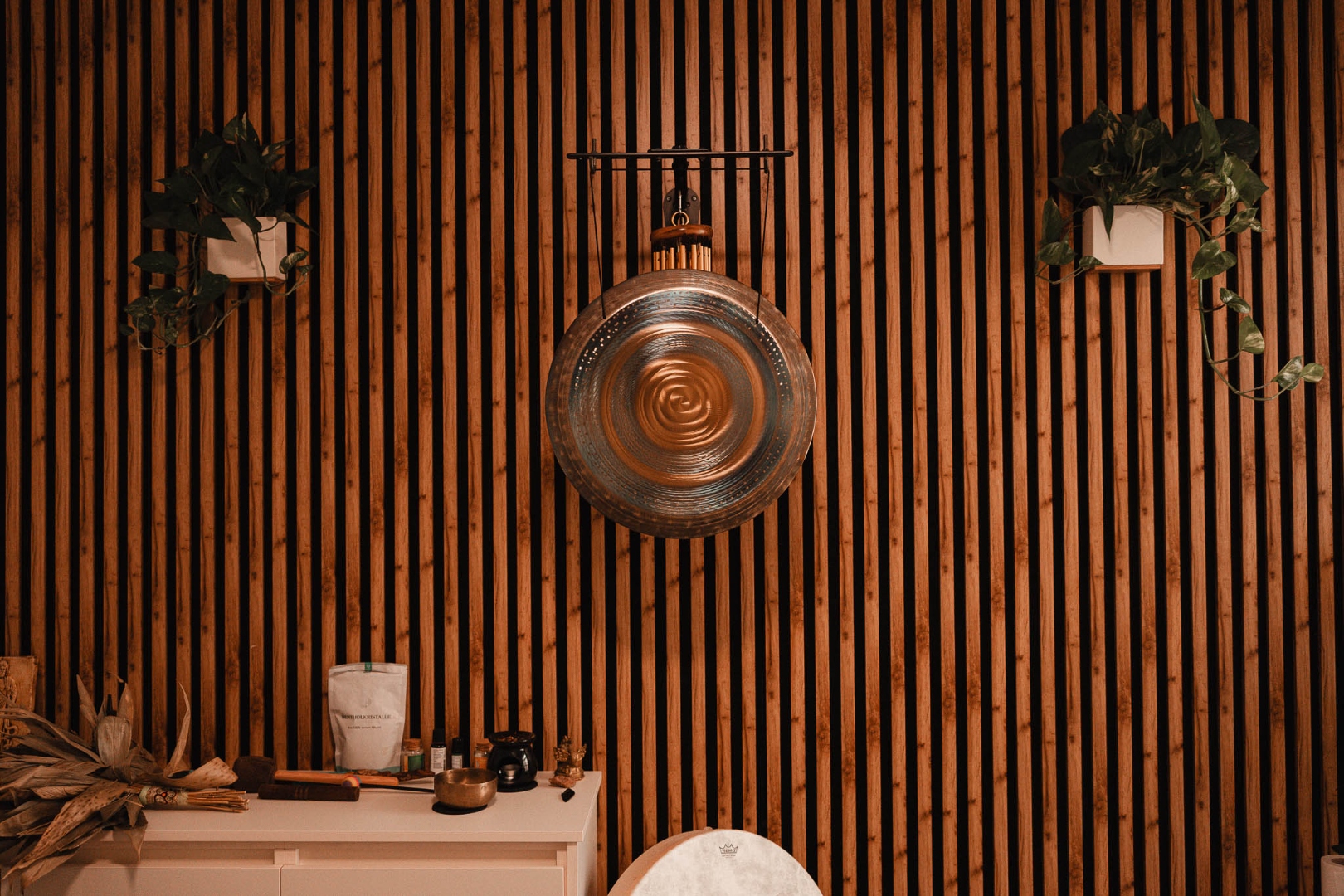 Bronze gong and wind chimes on a bamboo wall, flanked by trailing plants